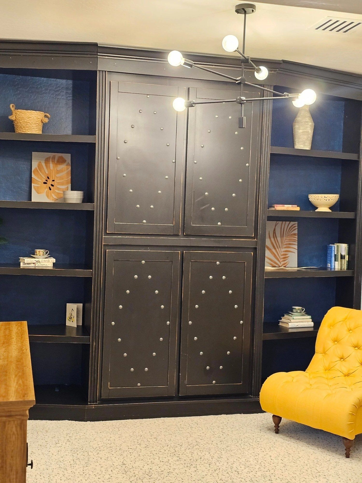 Den with a navy-backed bookcase, a modern chandelier, and a yellow armchair, freshly cleaned by Zita Cleaners Pro